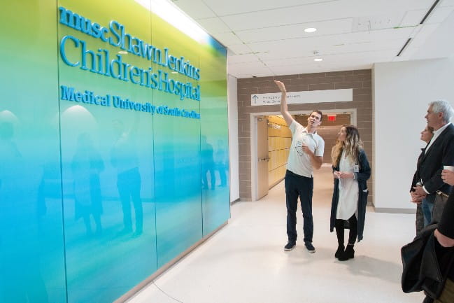 Artist gesturing to artwork on the wall of the Shawn Jenkins Children's Hospital