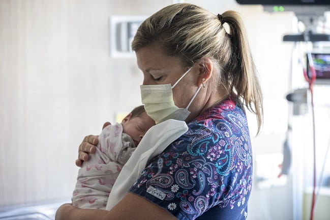 Care Team Member Nurse wearing a mask and holding an infant
