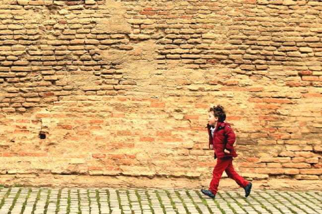 Young child running down cobblestone.