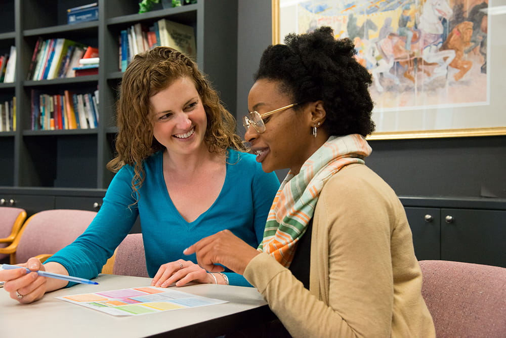 Two women sit together at a table and look at a document