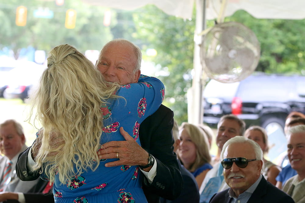 Two people hug as an audience under a tent looks on