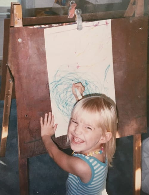 a young girl smiles as she look up from her art easel 