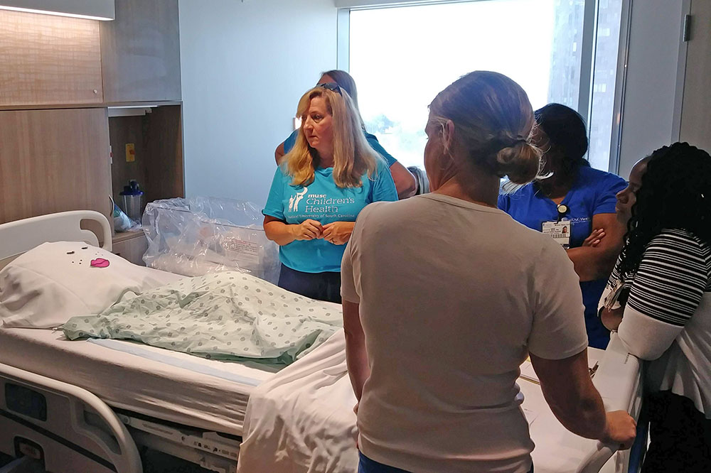 nurses stand around a dummy mother made with pillows and fake eyelashes in a new mother-baby room