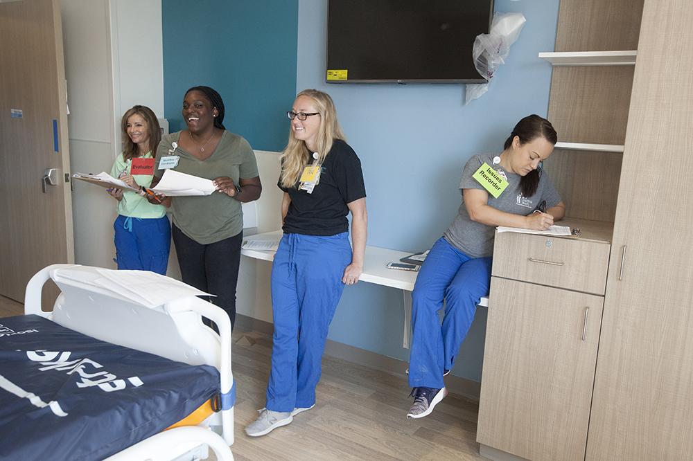 A team stands in a patient room with clipboards and records issues they find