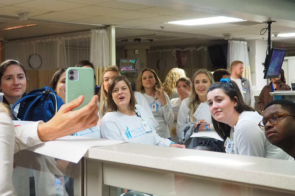 people gathered at a nurses station strain to watch a cellphone