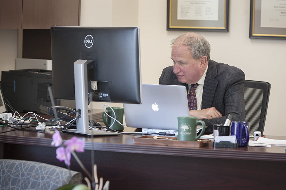 Dr. Leslie Lenert sits at his desk looking at several computer screens