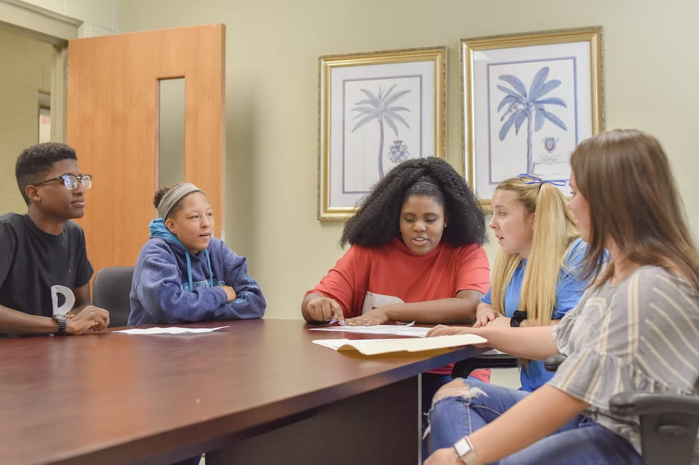 Five students sit around a table in a classroom