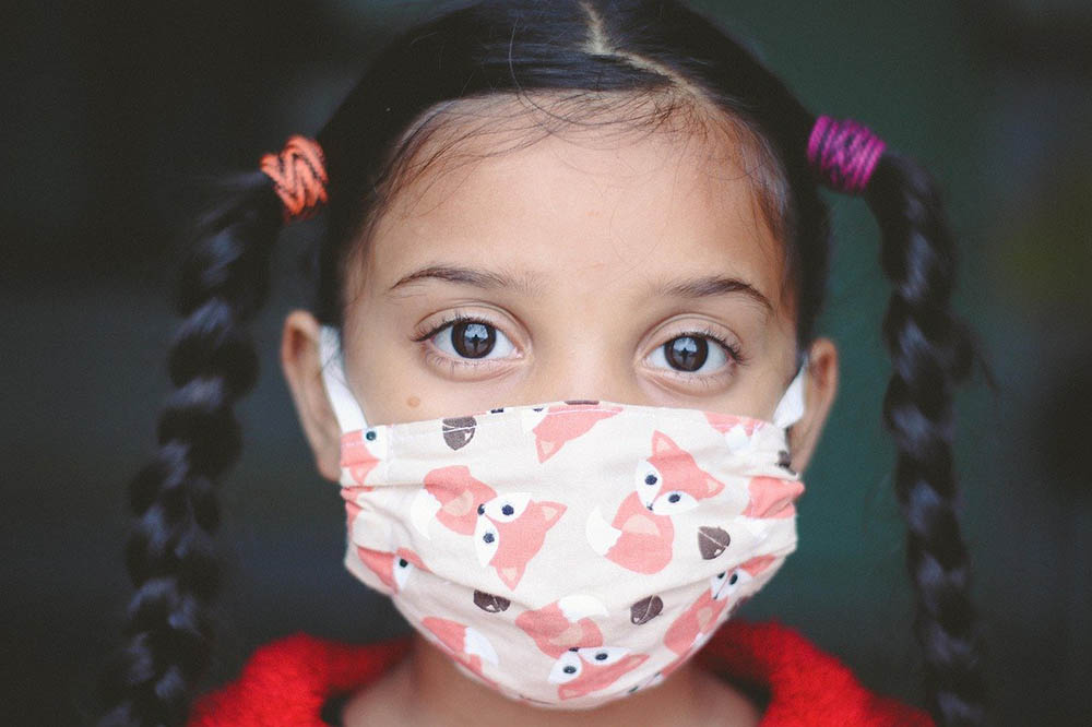closeup of girl with pigtail braids wearing a mask with pink foxes