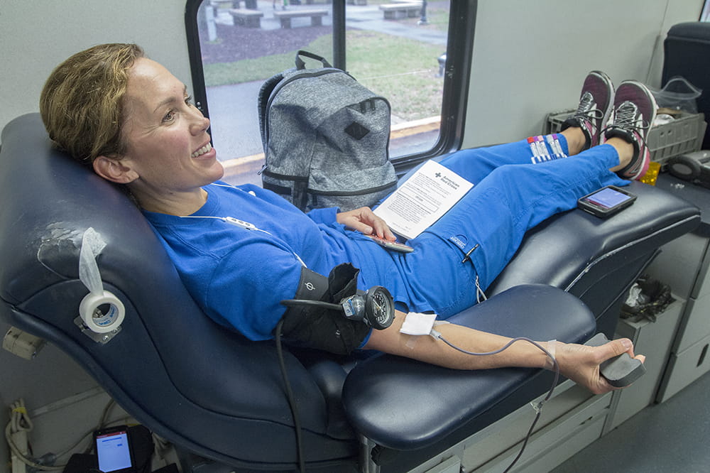  a woman in blue scrubs sits in a lounge chair while donating blood
