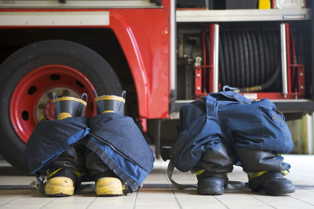 Two empty pairs of firefighter boots in front of fire truck