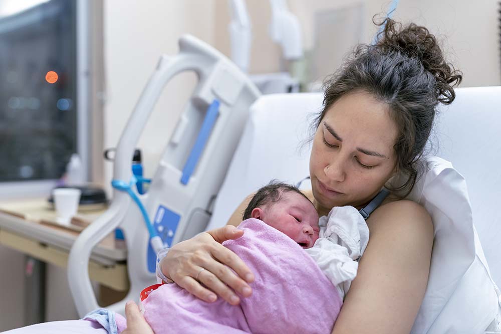Stock photo of woman with newborn baby under a pink blanket.