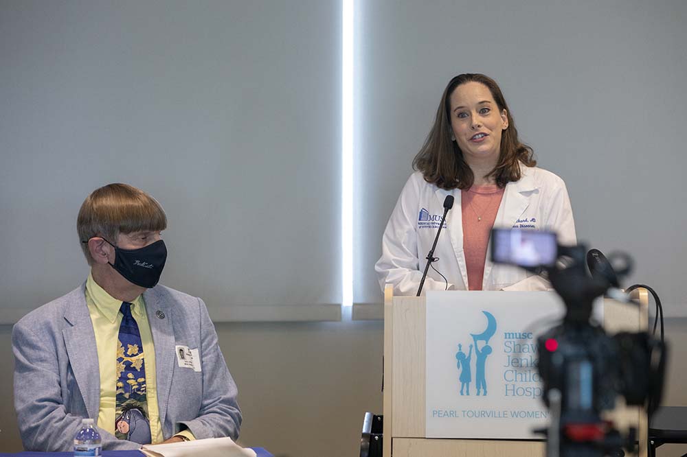 Dr. Allison Eckard stands at a podium while Dr. Edward Simmer, seated, listens.