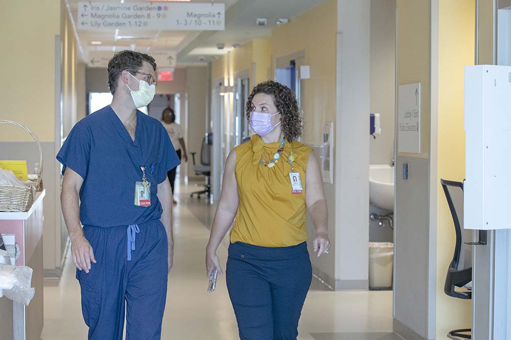A man in hospital scrubs talks with a woman while walking.