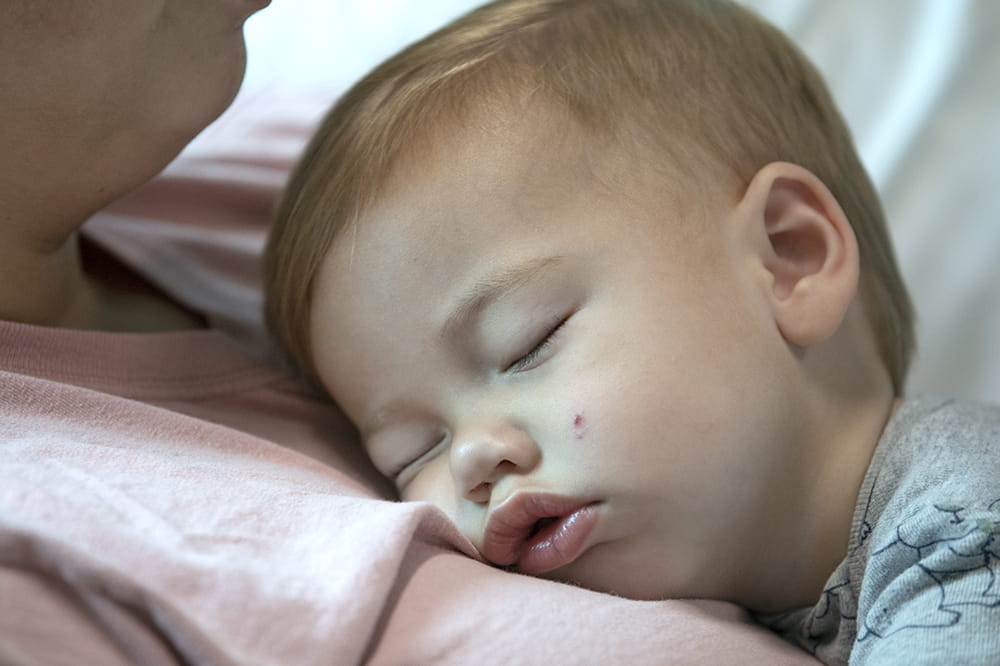 Closeup of little boy's face as he sleeps on his mother's chest.