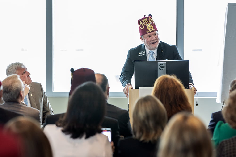 A Shriner wearing a cap speaks at a podium.