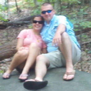 A man and woman sitting on a rock in the woods, smiling