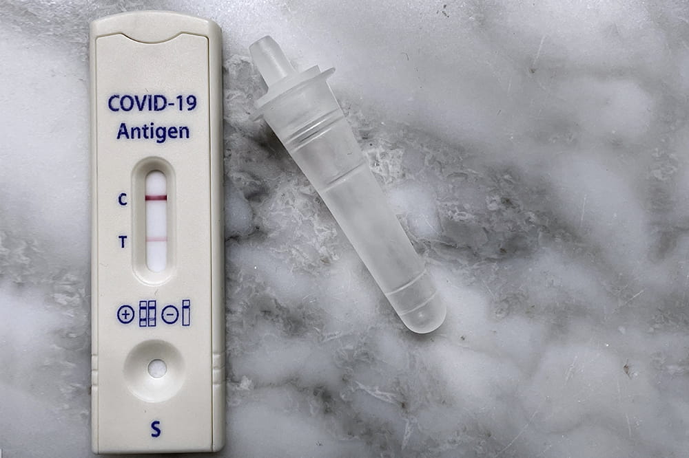 White rectangular COVID 19 test. It says COVID-19 antigen and has the letters C and T on the left side. There is a dark red line by the C and a fainter one by the T.
