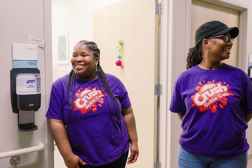 Two women wearing purple t-shirts with the words crush sickle cell on them.