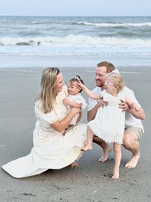 Two adults and two girls smile on a beach.