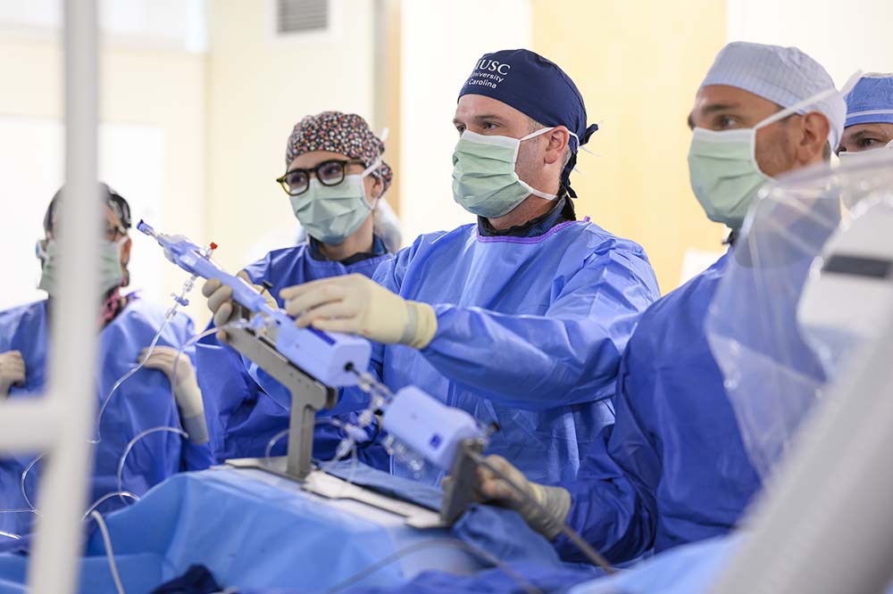 Five people in scrubs stand behind a medical device that is long and violet in color.