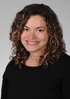 woman with brown curly hair wearing a black top smiles in a headshot.