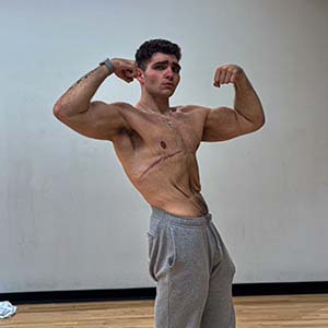 A young shirtless man flexes his muscles.