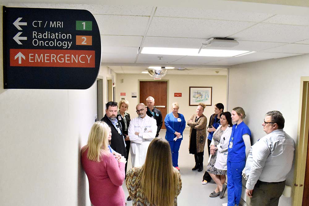 A sign points to the emergency department as a group of people gather in a hospital hallway.