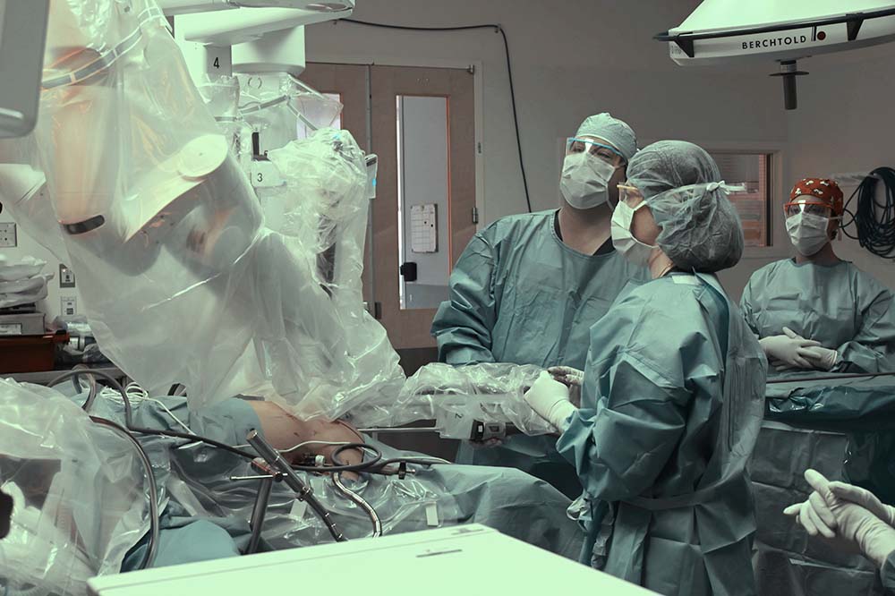 Photo of at least three people in an operating room with a robotic device.