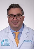 Headshot of man in white doctor's coat, yellow tie, blue short, He's wearing eyeglasses.