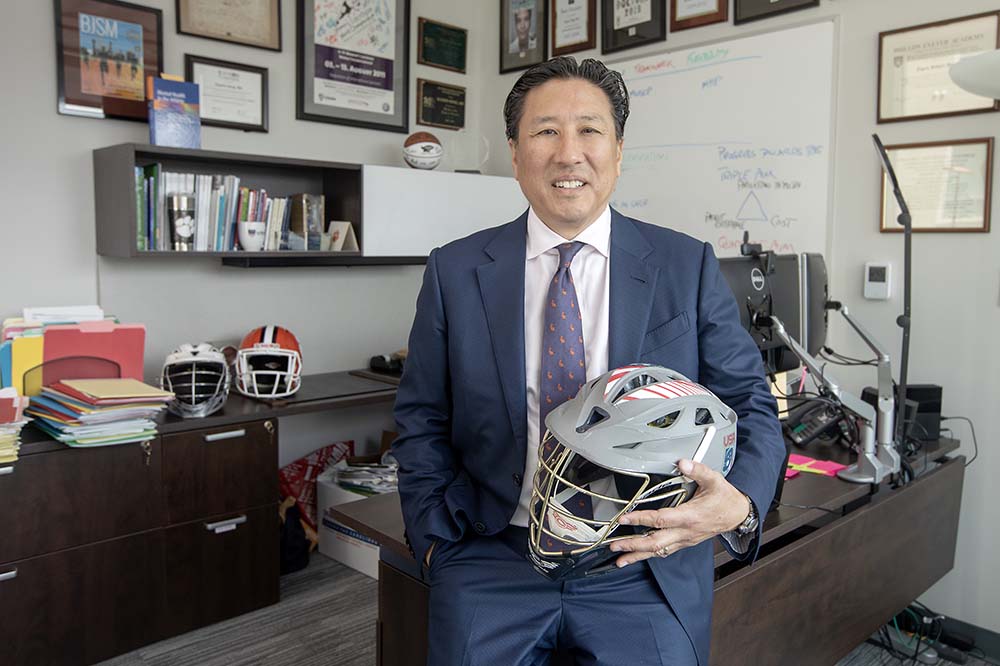 Smiling man wearing a suit holds a helmet as he sits on a desk.