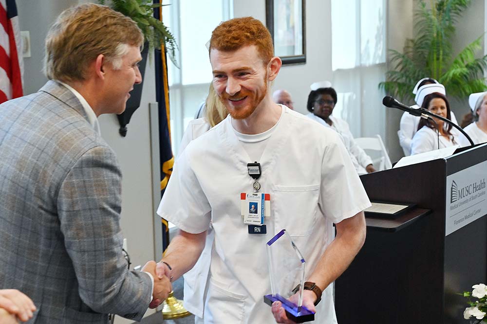 Smiling man with red hair and beard shakes hand of another man.