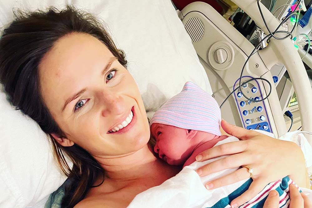 Beaming woman holds newborn baby.